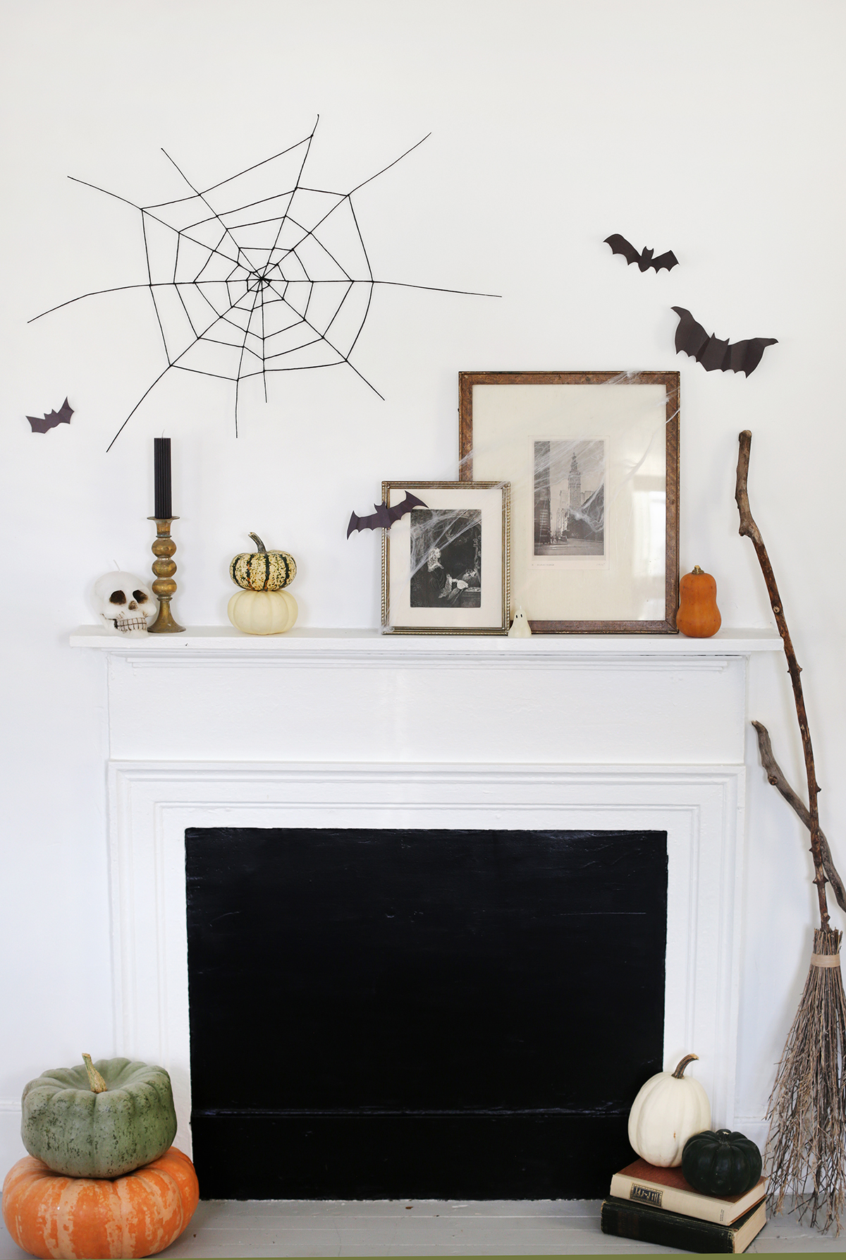 fireplace mantel with frames, pumpkins and surrounded by black bats on wall and black string spider web